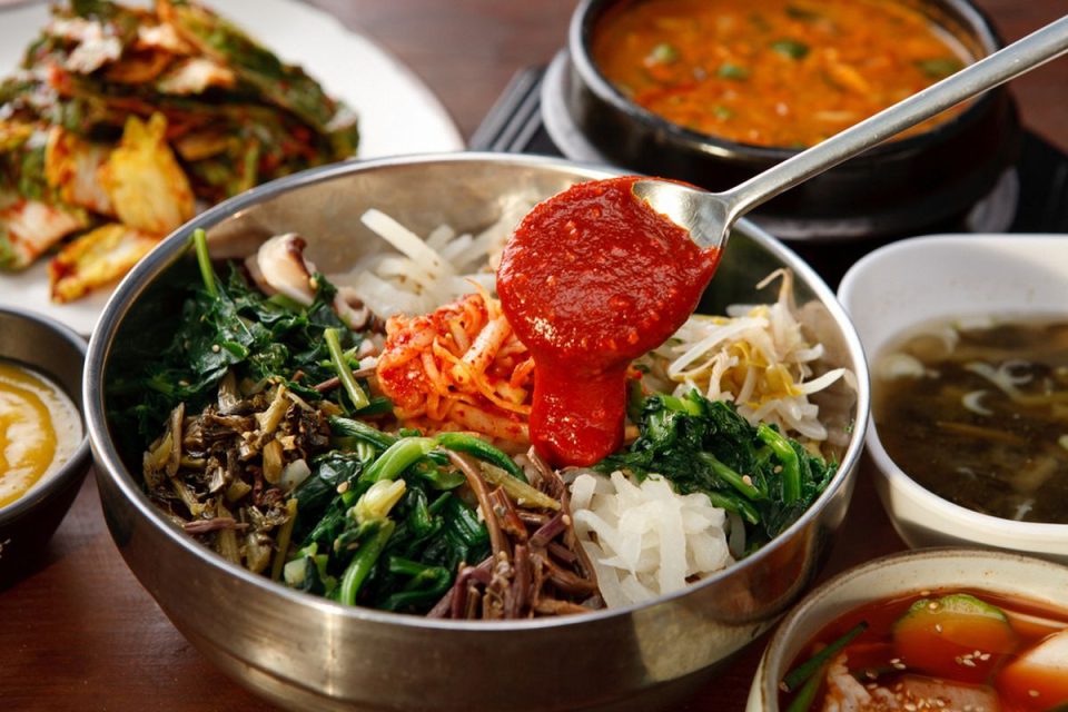 Seporsi bibimbap campur sayur dengan aneka warna sayuran segar, telur mata sapi, dan saus gochujang khas Korea