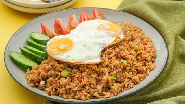 Semangkuk nasi goreng klasik lengkap dengan kerupuk, acar, dan irisan tomat segar